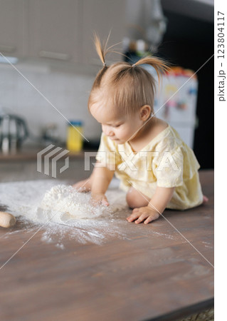 Toddler girl sitting on kitchen table, playfully scattering flour, capturing joyful moments of childhood exploration, vertical portrait, close-up, one person. Concept of simple pleasures childhood. Toddler girl sitting on kitchen table, playfully scattering flour, capturing joyful moments of childhood exploration, vertical portrait, close-up, one person. Concept of simple pleasures childhood. 123804117