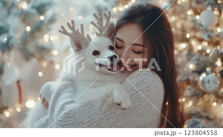 Happy Holidays: Woman Hugs Cute Dog In Reindeer Antlers By Stylish Christmas Tree In Festive Room, Celebrating Winter Together. Happy Holidays: Woman Hugs Cute Dog In Reindeer Antlers By Stylish Christmas Tree In Festive Room, Celebrating Winter Together. 123804558