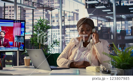 Chief executive officer calling her secretary on office landline phone, asking about important paperwork to solve business tasks for development. African american boss does task management. Camera B. Chief executive officer calling her secretary on office landline phone, asking about important paperwork to solve business tasks for development. African american boss does task management. Camera B. 123807985