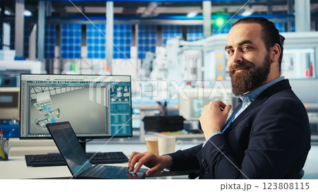 Employee in renewable energy based factory using laptop to review performance of robot arms placing solar panels. Specialist inspects machinery placing solar cells on conveyor belts, camera A Employee in renewable energy based factory using laptop to review performance of robot arms placing solar panels. Specialist inspects machinery placing solar cells on conveyor belts, camera A 123808115