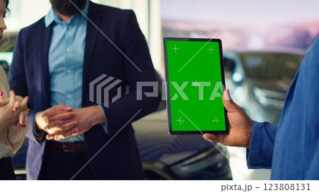 Salesman using green screen tablet to present car addons options to clients, trying to sway them make purchase. Showroom agent offers extended warranty to customers, holding mockup device, camera A Salesman using green screen tablet to present car addons options to clients, trying to sway them make purchase. Showroom agent offers extended warranty to customers, holding mockup device, camera A 123808131