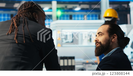 Solar panels plant expert talks with business partner about developing technologies harnessing sun power. Photovoltaics factory researcher brainstorms with colleague to improve efficiency, camera B 123808144