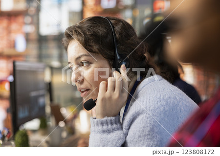 Customer service employee talking in headset mic, tracking support ticket in dedicated company software on PC. Call center worker creating support ticket for customer calling to solve issue 123808172