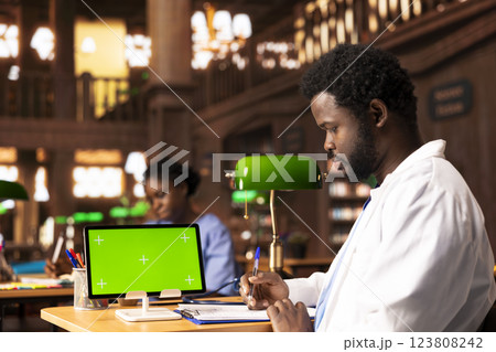 African american student learning to become a doctor next to copy space, taking notes after studying research papers. Young man future doctor sitting at the campus library, med school. African american student learning to become a doctor next to copy space, taking notes after studying research papers. Young man future doctor sitting at the campus library, med school. 123808242