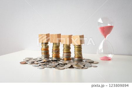 4 blank square blocks on top of stacked coins with sand timer. 4 blank square blocks on top of stacked coins with sand timer. 123809894