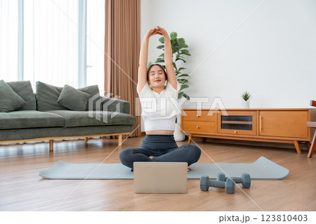 Happy young Asian woman practicing yoga and shoulder stretching at home 123810403