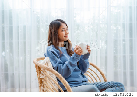 Young Asian woman happy and smiling, sitting on seat and holding mug in living room at home 123810520