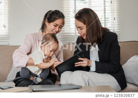 Two women and a baby in a home setting, discussing business with a tablet, showcasing work-life balance and modern family dynamics. 123810837