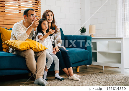 A cheerful Asian family finds relaxation and joy while watching TV at home. The father mother son and daughter share moments of happiness creating cherished family memories during their weekend. A cheerful Asian family finds relaxation and joy while watching TV at home. The father mother son and daughter share moments of happiness creating cherished family memories during their weekend. 123814850