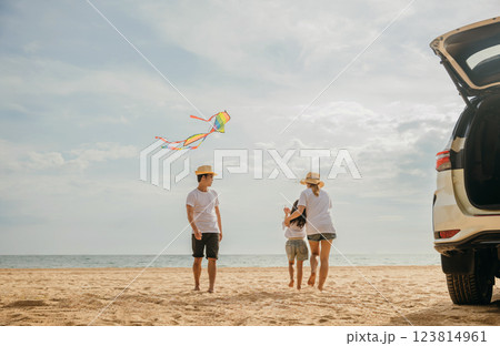 Asian family is flying a kite while running on the beach. Happy parents mother and father with their child playing with kite, The car is parked nearby, and the family is enjoying their time together 123814961