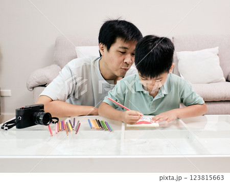 Asian caring father watches his young son draw with colored pencils, sharing creative and educational moment together at home 123815663