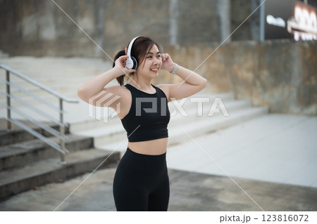 Joyful Asian young woman wearing wireless headphones while exercising outdoors in stylish athletic wear, enjoying music during her active lifestyle routine Joyful Asian young woman wearing wireless headphones while exercising outdoors in stylish athletic wear, enjoying music during her active lifestyle routine 123816072