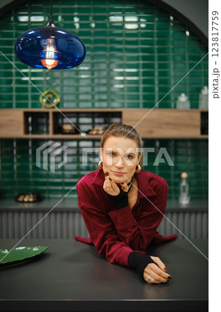 A woman is leaning on a kitchen counter, wearing a red outfit with long sleeves A woman is leaning on a kitchen counter, wearing a red outfit with long sleeves 123817759