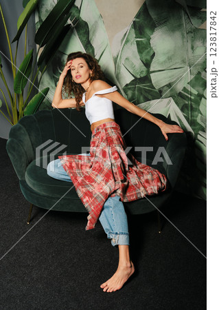 Adult woman lounging gracefully on a velvet sofa against a leafy backdrop Adult woman lounging gracefully on a velvet sofa against a leafy backdrop 123817842