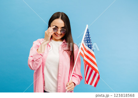Young smiling happy woman wears casual clothes holding american flag and looking to the camera isolated on blue color background. 123818568