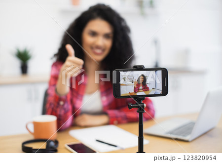 Young African woman with curly hair creating video content at home using smartphone tripod for vlog. Scene emphasizes creativity, technology, and online communication. . Young African woman with curly hair creating video content at home using smartphone tripod for vlog. Scene emphasizes creativity, technology, and online communication. . 123820954