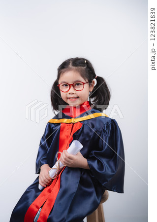 Happy Asian Asian Young Girl in Graduation Gown Holding Diploma and Smiling at Camera Against Plain Background 123821839