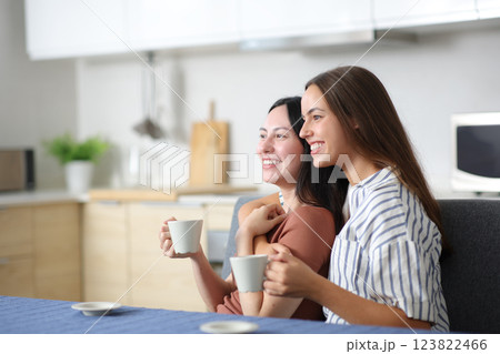 Happy interracial lesbian couple drinking and contemplating in the kitchen Happy interracial lesbian couple drinking and contemplating in the kitchen 123822466