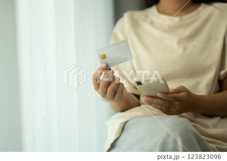 Close up of woman holding credit card and using smartphone for an online transaction 123823096
