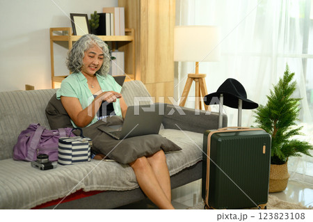 Happy older woman checking travel plans on her laptop before summer trip Happy older woman checking travel plans on her laptop before summer trip 123823108