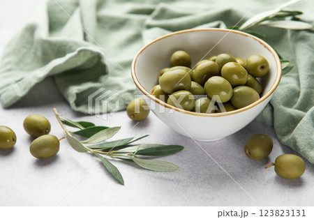 Green olives served in white ceramic bowl on marble table with olive branches Green olives served in white ceramic bowl on marble table with olive branches 123823131