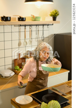 Senior woman smelling food in a frying pan while cooking in the kitchen 123823154