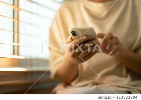 Close up of a woman using smartphone, sitting near a window with wooden blinds Close up of a woman using smartphone, sitting near a window with wooden blinds 123823204
