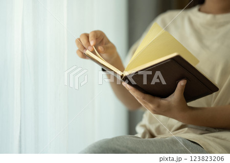 Young woman flipping through the pages of brown leather notebook while sitting near a window 123823206