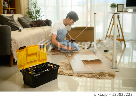 Focused young asian man assembling new furniture in his living room 123823222