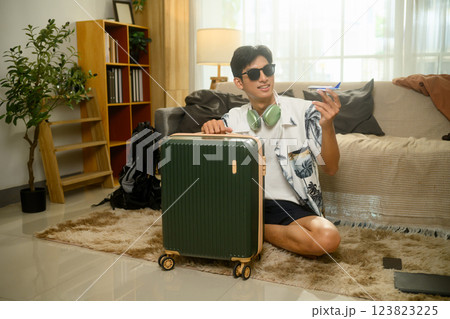 Young man excited for a summer trip, sitting on floor with luggage and holding a toy airplane 123823225