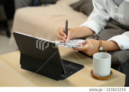 Cropped shot of woman taking notes in a notebook and working on a digital tablet. 123823258