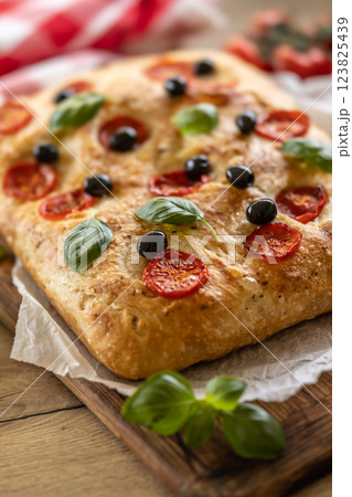Focaccia - Italian Bread with tomatoes basil leaves olives and olive oil on cutting board Focaccia - Italian Bread with tomatoes basil leaves olives and olive oil on cutting board 123825439