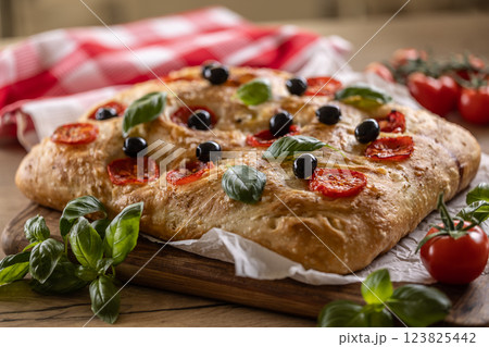 Focaccia - Italian Bread with tomatoes basil leaves olives and olive oil on cutting board 123825442