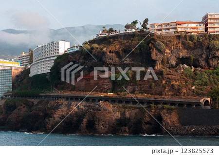 Dramatic oceanfront cliffs with modern buildings and lush vegetation under a cloudy sky Dramatic oceanfront cliffs with modern buildings and lush vegetation under a cloudy sky 123825573