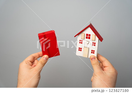 Man holds a miniature house and gift box. Housing as a gift. Win an apartment in the lottery. To inherit property. Holiday discounts. Buying an apartment at a low price. Sale of real estate. Present 123827180