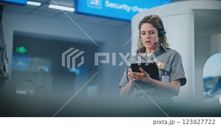 Female TSA Officer with Tablet Computer Wearing Headset Instructs Airport Staff Female TSA Officer with Tablet Computer Wearing Headset Instructs Airport Staff 123827722