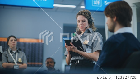 Female TSA Officer with Tablet Computer Wearing Headset Instructs Airport Staff 123827729