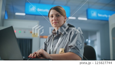 Airport Security: Female TSA Officer Using Laptop, Smiling and Looking at Camera 123827744