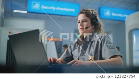 Airport Security Checkpoint: Female TSA Officer Wearing Headset Works on Laptop Airport Security Checkpoint: Female TSA Officer Wearing Headset Works on Laptop 123827754
