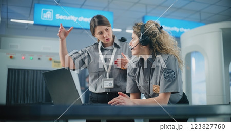 Female TSA Officer Wearing Headset Uses Laptop, Discusses Security Issues with Colleague 123827760