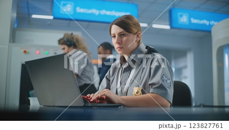 Airport Security: Female TSA Officer Using Laptop, Smiling and Looking at Camera 123827761