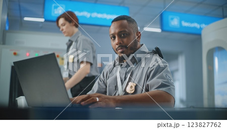 Airport Security Checkpoint: Security Officer Using Laptop Computer, Looking at Camera 123827762