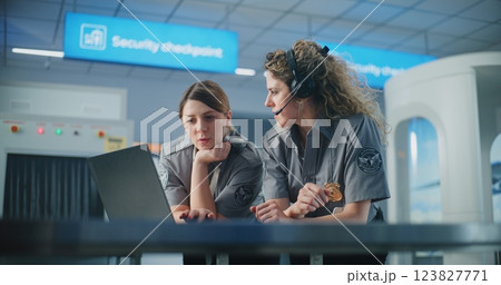 Airport Security Checkpoint: Two Female TSA Officers in Headset Using Laptop Computer and Talking 123827771