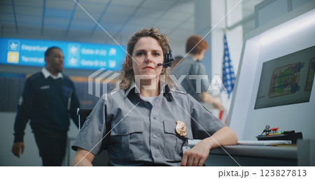 Portrait of Female Security Officer Sitting at Control Panel of X-ray Scanner, Looking at Camera 123827813