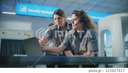 Airport Security Checkpoint: Two Female TSA Officers in Headset Using Laptop Computer and Talking Airport Security Checkpoint: Two Female TSA Officers in Headset Using Laptop Computer and Talking 123827817