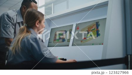 Two TSA Workers Controlling X-ray Scanning of Suitcase on Computer Monitors 123827966
