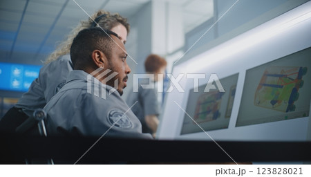 Two Security Officers Analyzing X-ray Scanning Images of Baggage on Computer Screens 123828021