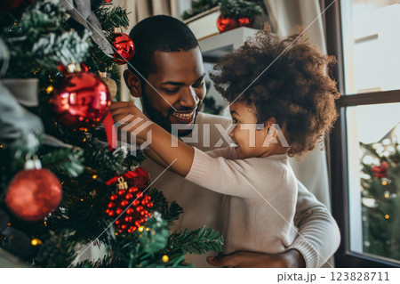 Father and daughter are spending quality time together, decorating a Christmas tree with red ornaments. They are smiling and enjoying the festive atmosphere 123828711