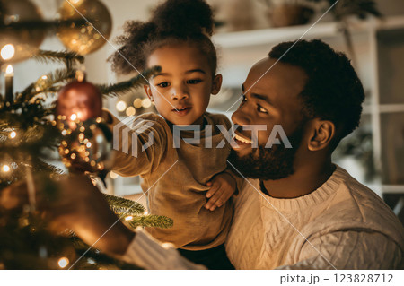 Father and daughter are sharing a special moment while decorating the Christmas tree with sparkling ornaments and twinkling lights 123828712