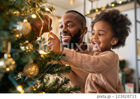 Dad and his young daughter are enjoying spending time together decorating a Christmas tree with sparkling lights 123828713